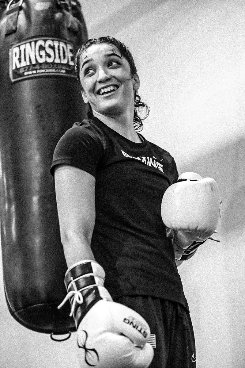 Idaho native Alyssa Mendoza smiles, wearing boxing gloves and standing in front of a punching bag.