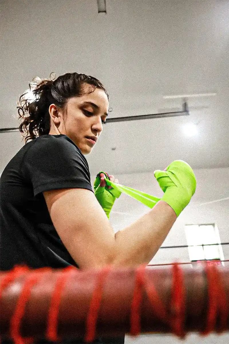 Alyssa Mendoza prepares to box by putting on green hand wraps.