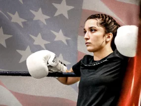 Alyssa Mendoza stands in a boxing ring with an American flag in the background.