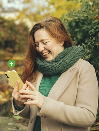 A lady wearing a green scarf looking at her phone with a plus sign above it