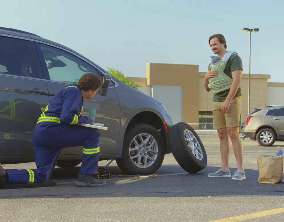 A father carrying a baby while getting roadside assistance on their car