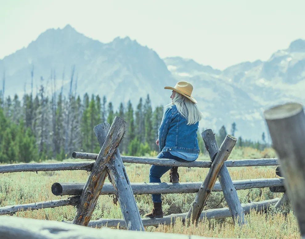 A woman sitting on a wooden fence while looking at the mountains